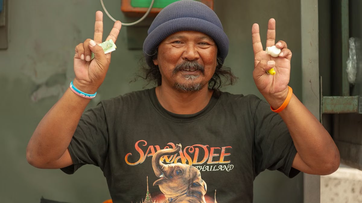 Smiling man in Thailand T-shirt flashing peace signs.