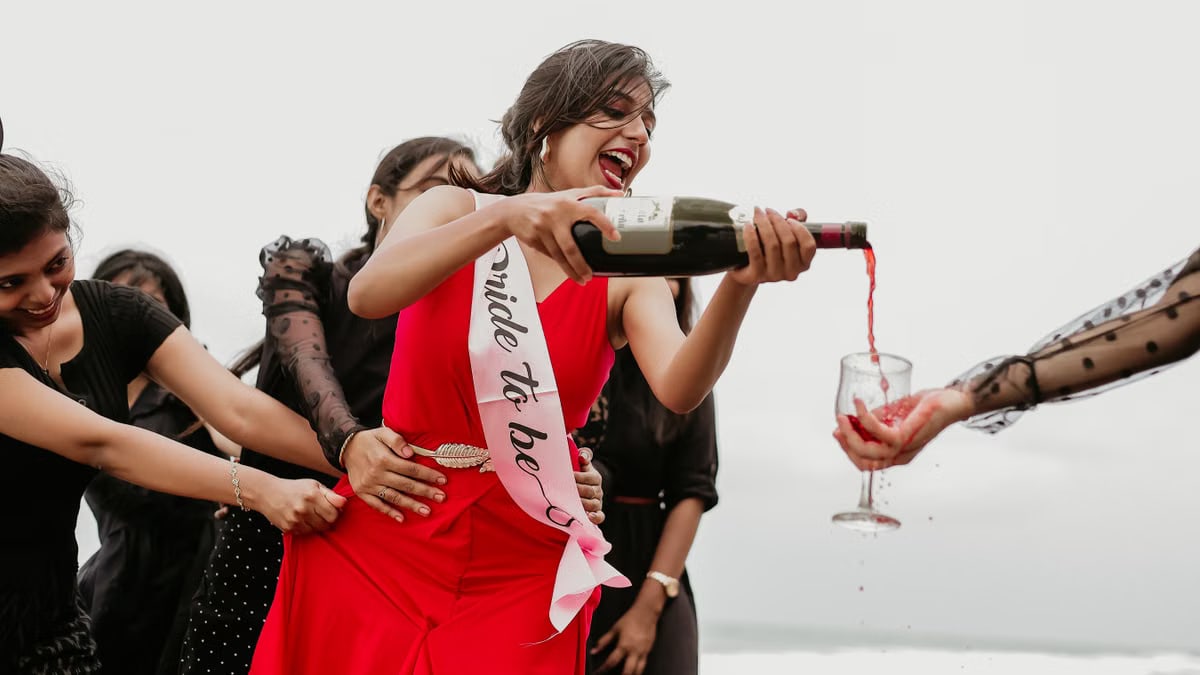 Joyful bride-to-be celebrating with friends, pouring red wine outdoors in vibrant atmosphere.
